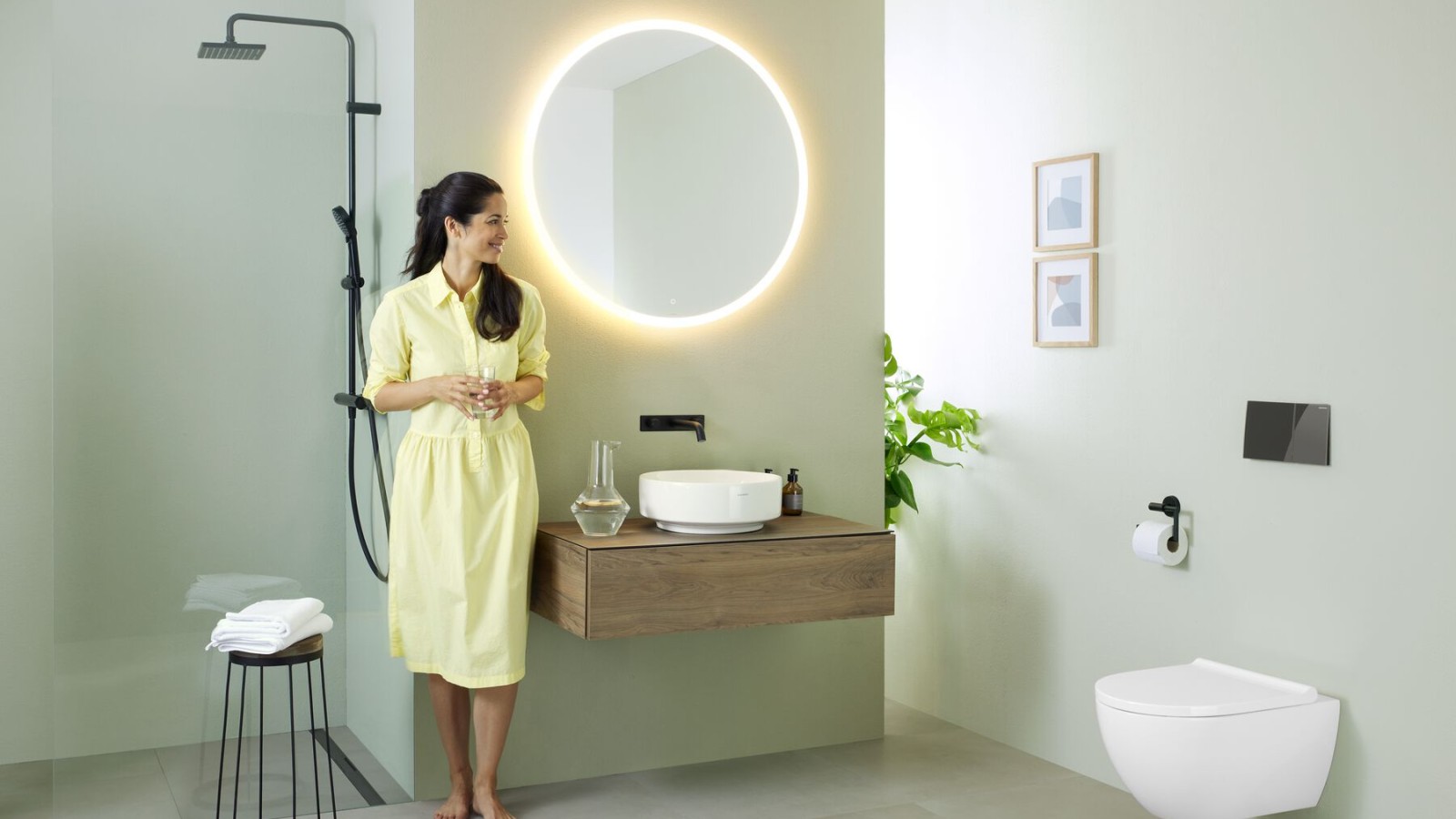Woman in yellow dress standing in front of mint green bathroom with furniture and bathroom ceramics from Geberit and black taps Woman in yellow dress standing in front of mint green bathroom with furniture and bathroom ceramics from Geberit and black taps
