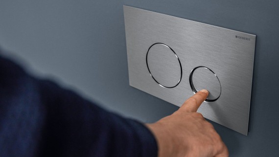 Hand actuates small flush at the Sigma40 Round actuator plate (© Geberit)