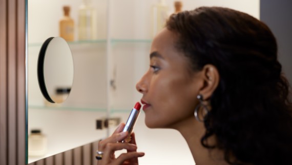 Woman applying lipstick in front of a magnifying mirror (© Geberit)