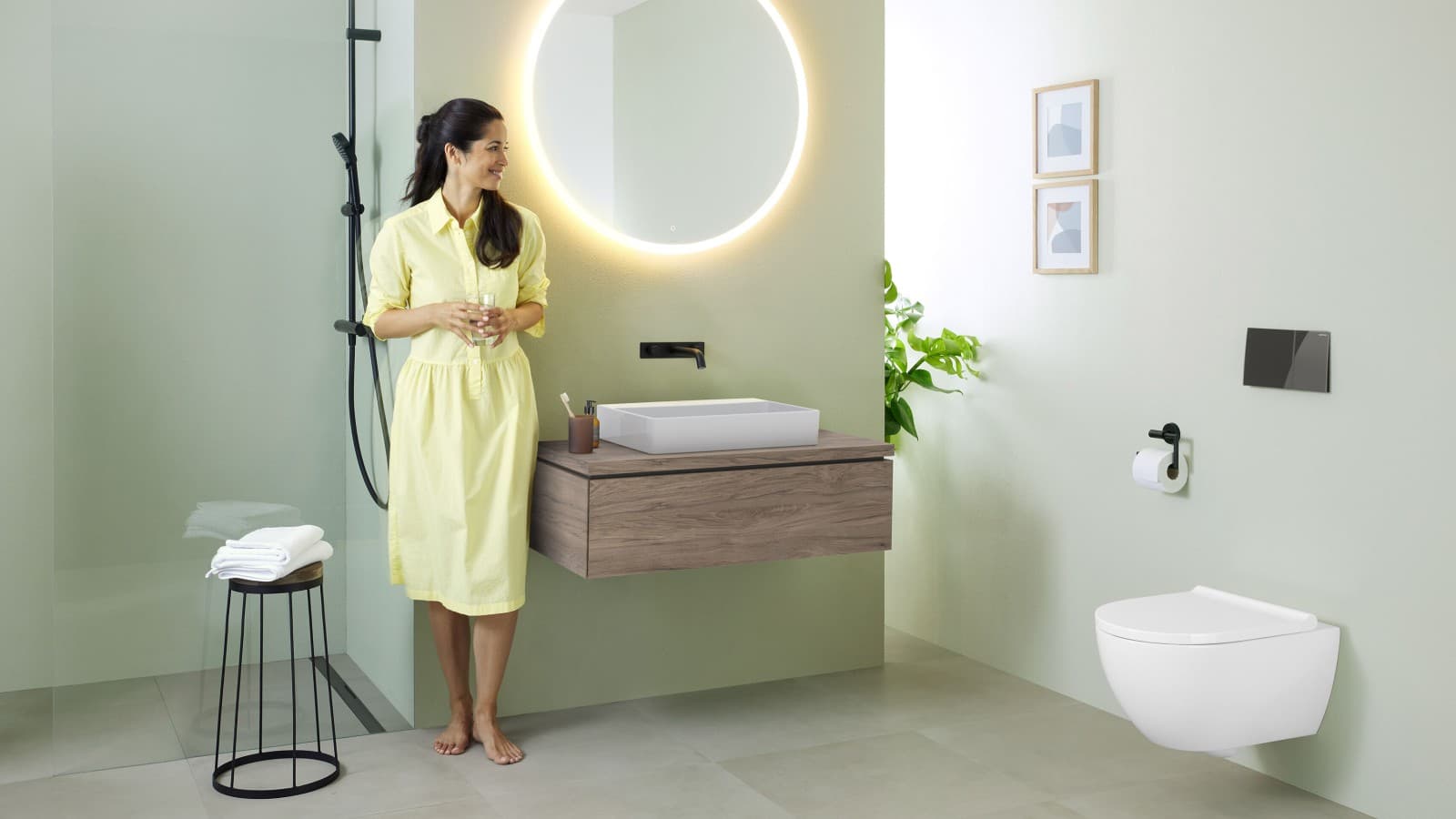 Woman in yellow dress standing in front of mint green bathroom with furniture and bathroom ceramics from Geberit and black taps Woman in yellow dress standing in front of mint green bathroom with furniture and bathroom ceramics from Geberit and black taps