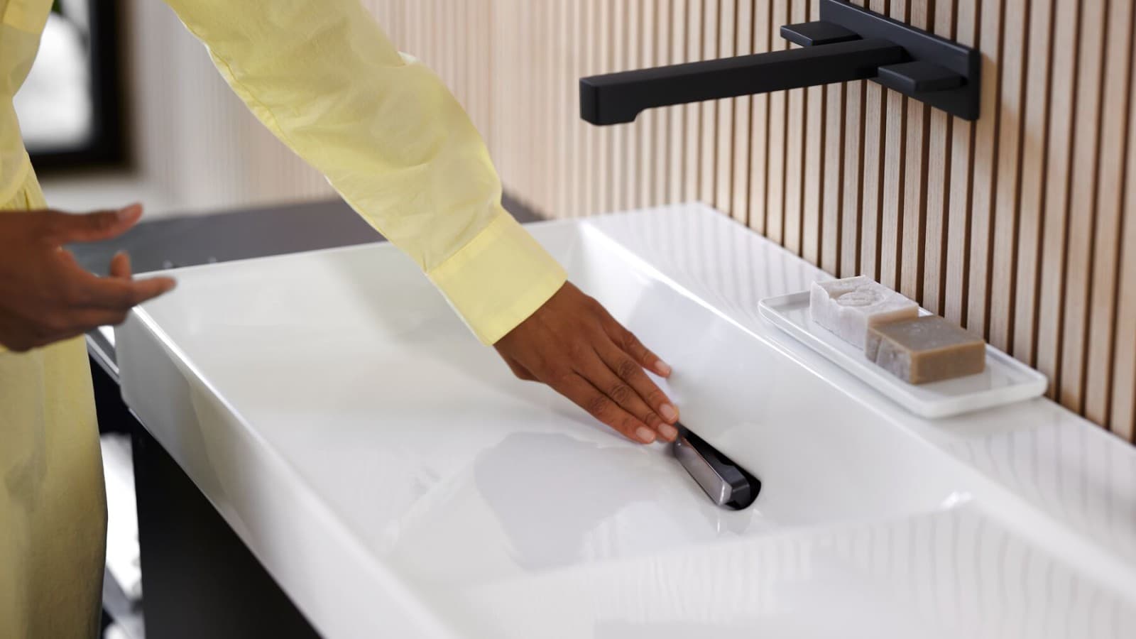 Woman removes comb insert on Geberit ONE washbasin with tap in black matt. (© Geberit) Woman removes comb insert on Geberit ONE washbasin with tap in black matt. (© Geberit)